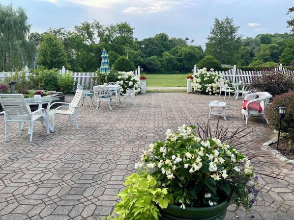 An outdoor patio with white wicker furniture, a fountain, and a white picket fence.