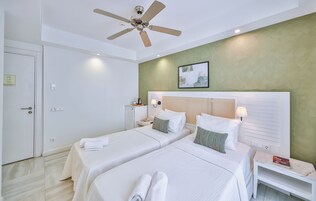 Habitación de hotel con dos camas, un ventilador de techo, una mesita de noche con lámpara y un cuadro enmarcado en la pared.