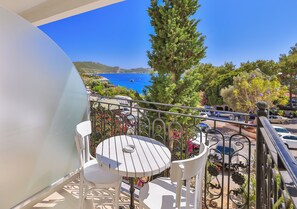 Un balcón con una mesa y sillas blancas, con vistas a una zona costera con barcos y vegetación.