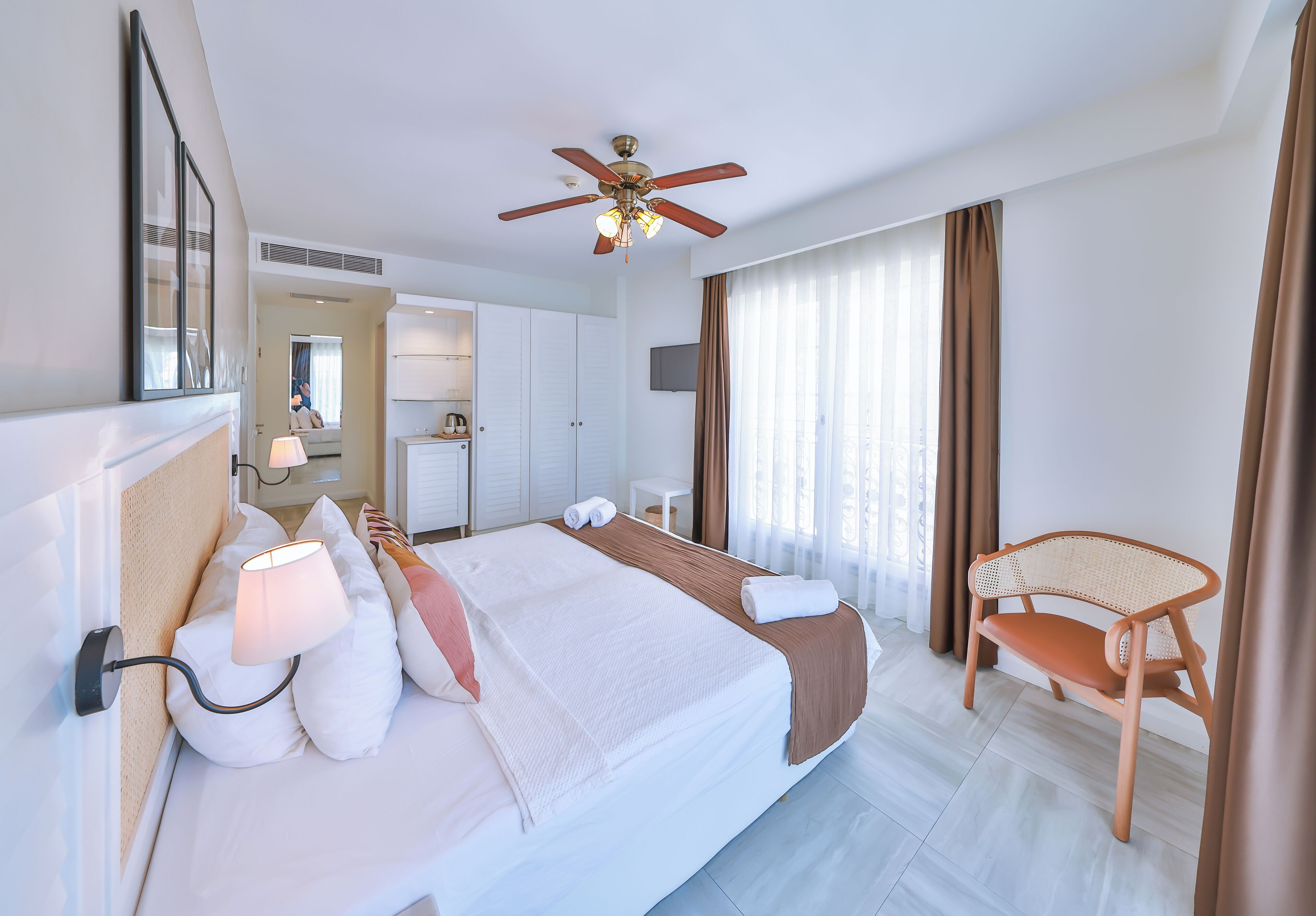A hotel room with a bed, a ceiling fan, a desk, and a chair.
