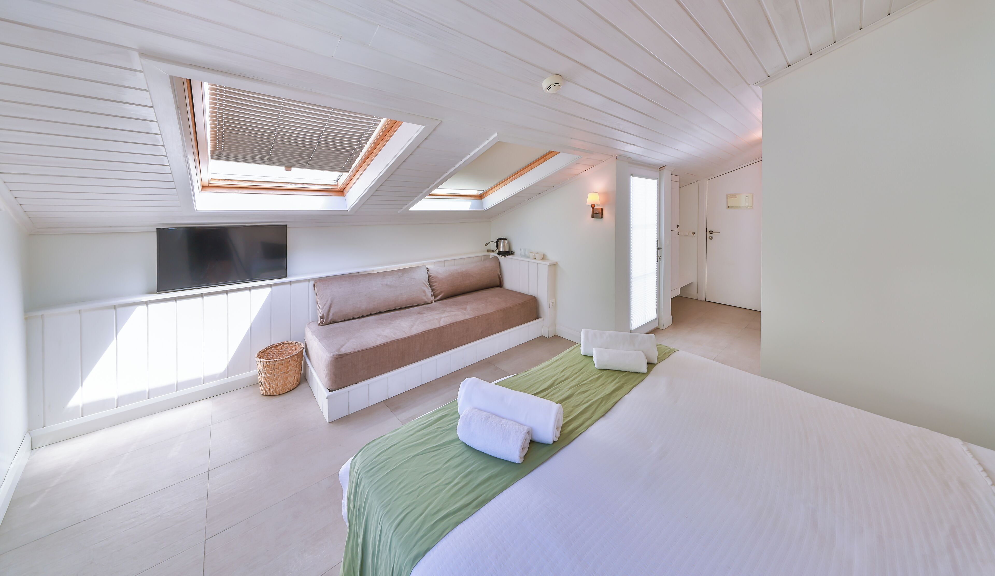 Una habitación con cama, sofá, televisión y tragaluces.