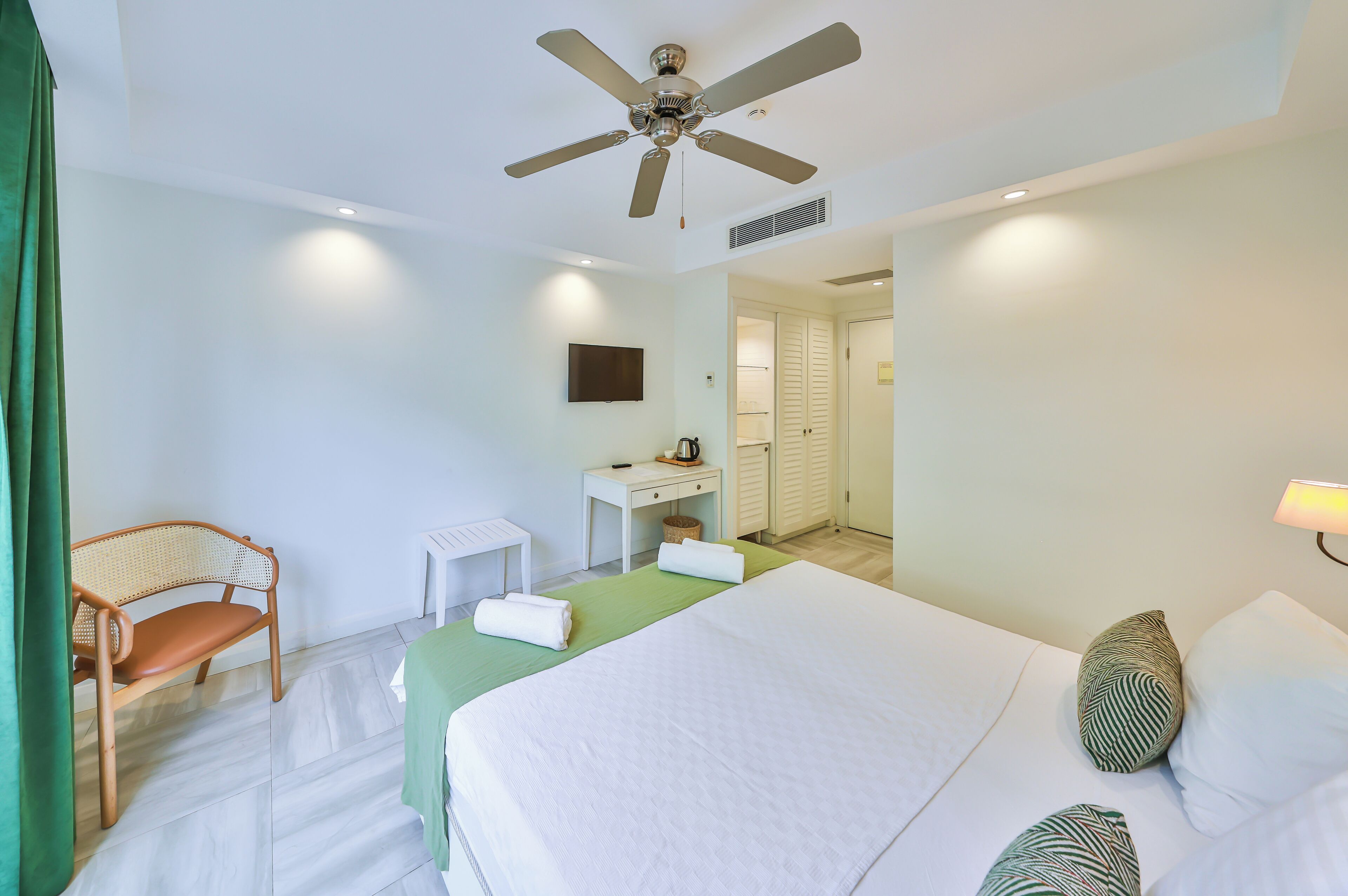 Una habitación de hotel con cama, escritorio, silla, ventilador de techo y televisor.