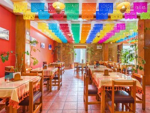 A restaurant with wooden tables and chairs, red walls, and colorful paper decorations hanging from the ceiling. - OYO Hotel Mi casa, Oaxaca centro (Oaxaca)