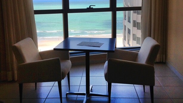 A room with a view of the ocean through large windows, two chairs, and a small table. - Eninova Flat Executive (Recife)