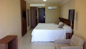 A hotel room with two beds, a TV, an air conditioner, a lamp, and a checkered rug. - Eninova Flat Executive (Recife)