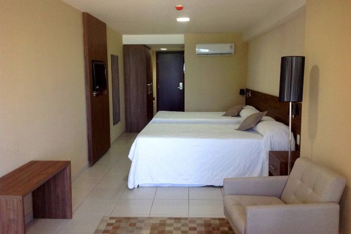 Habitación de hotel con dos camas, televisión, aire acondicionado, lámpara y alfombra a cuadros.