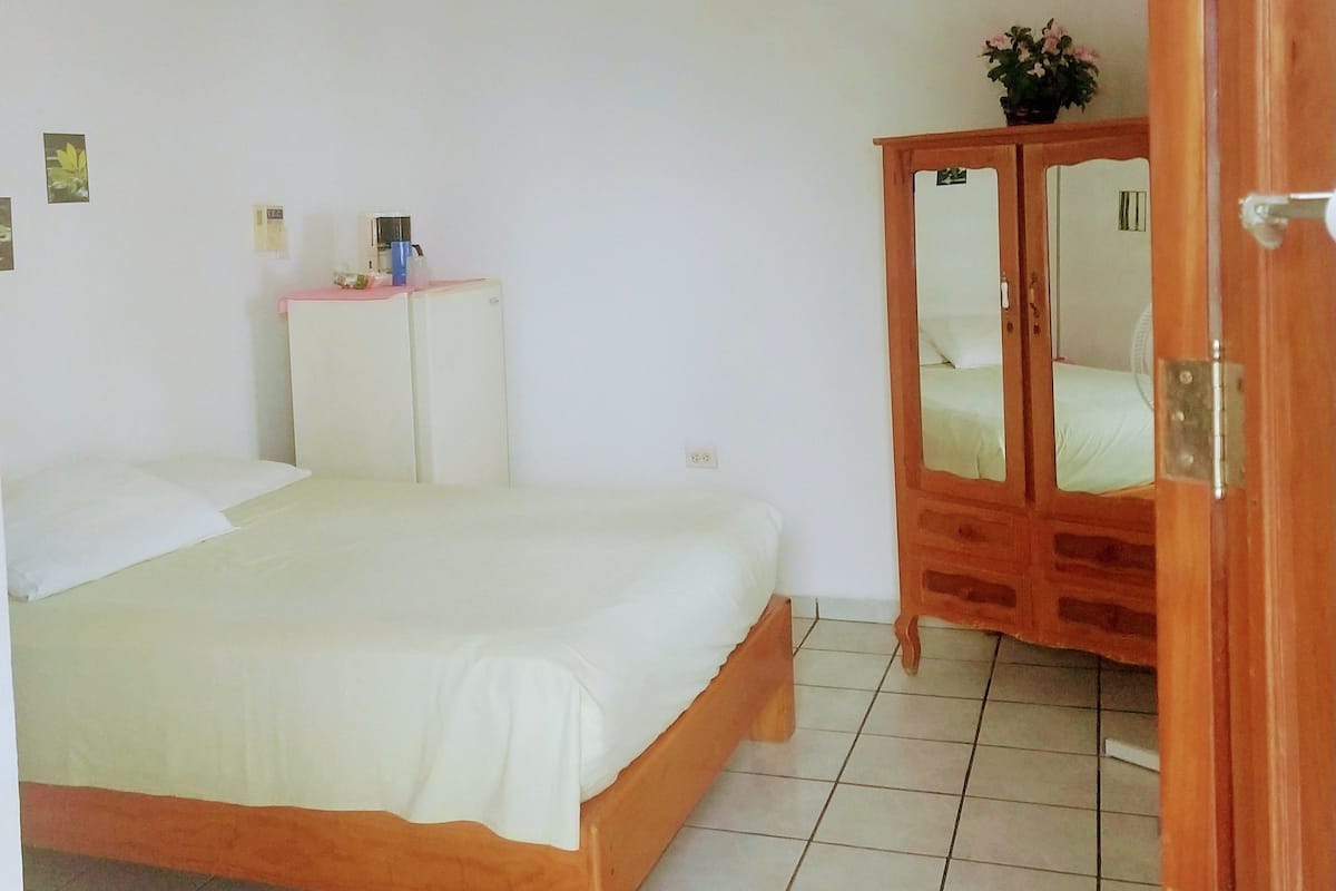 A bedroom with a bed, a wardrobe, a ceiling fan, and a tiled floor.
