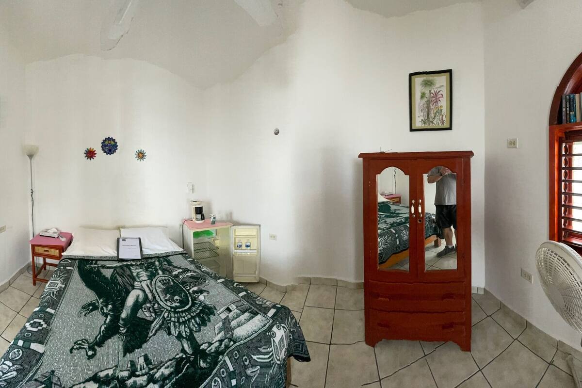 A room with a bed, a desk, a wardrobe, and a fan.