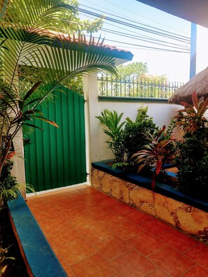 A covered outdoor area with a green gate, potted plants, and a tiled floor.