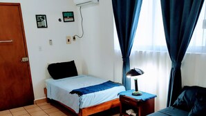 Un dormitorio con dos camas, una puerta de madera, un equipo de aire acondicionado y una mesita de noche con lámpara.
