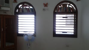 Dos ventanas con estanterías encima, un ventilador de pared y un armario de madera.