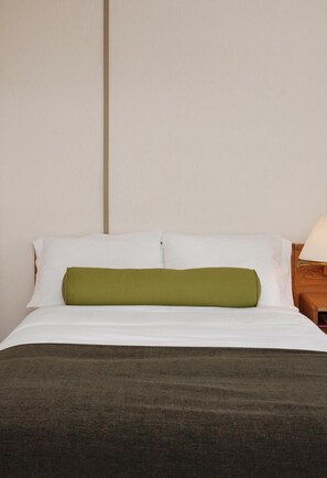 A neatly made bed with white and green bedding, a wooden nightstand with a lamp, and a plain wall.