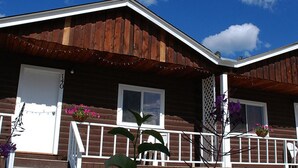 A wooden cabin with a porch, white railings, and flower baskets. - Triple J Hotel & Cabins (Dawson City)