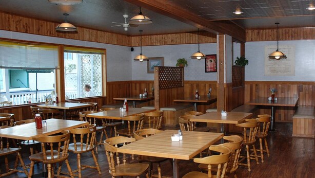 A restaurant with wooden tables and chairs, ceiling fans, and a menu board on the wall. - Triple J Hotel & Cabins (Dawson City)