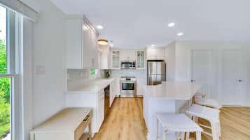 A modern kitchen with white cabinetry, stainless steel appliances, and a wooden floor.