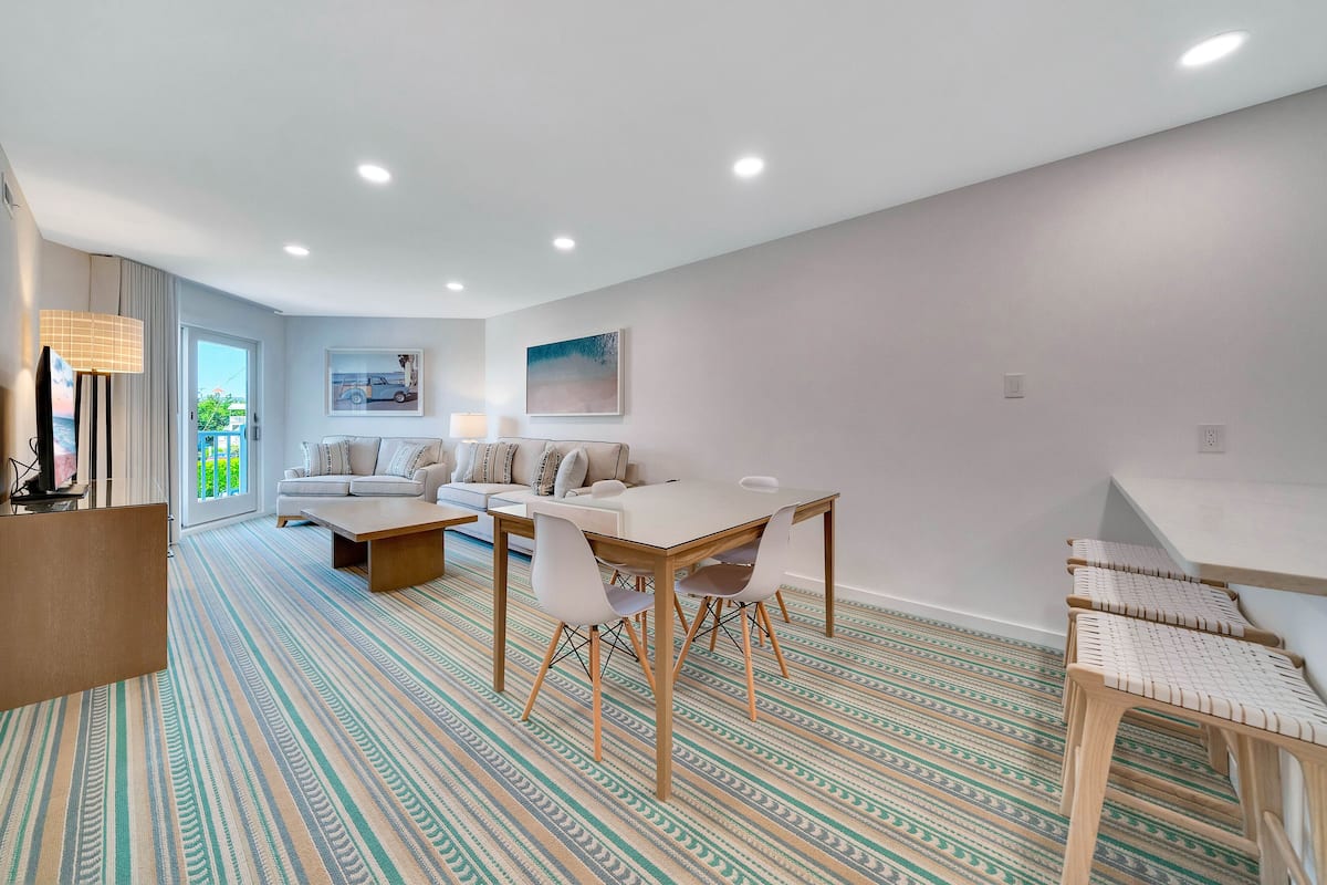 A modern living room with a dining area, a sofa set, and a patterned carpet.