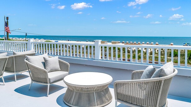 A balcony with wicker furniture, a view of the ocean, and a white railing.