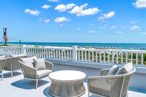A balcony with wicker furniture, a view of the ocean, and a white railing.