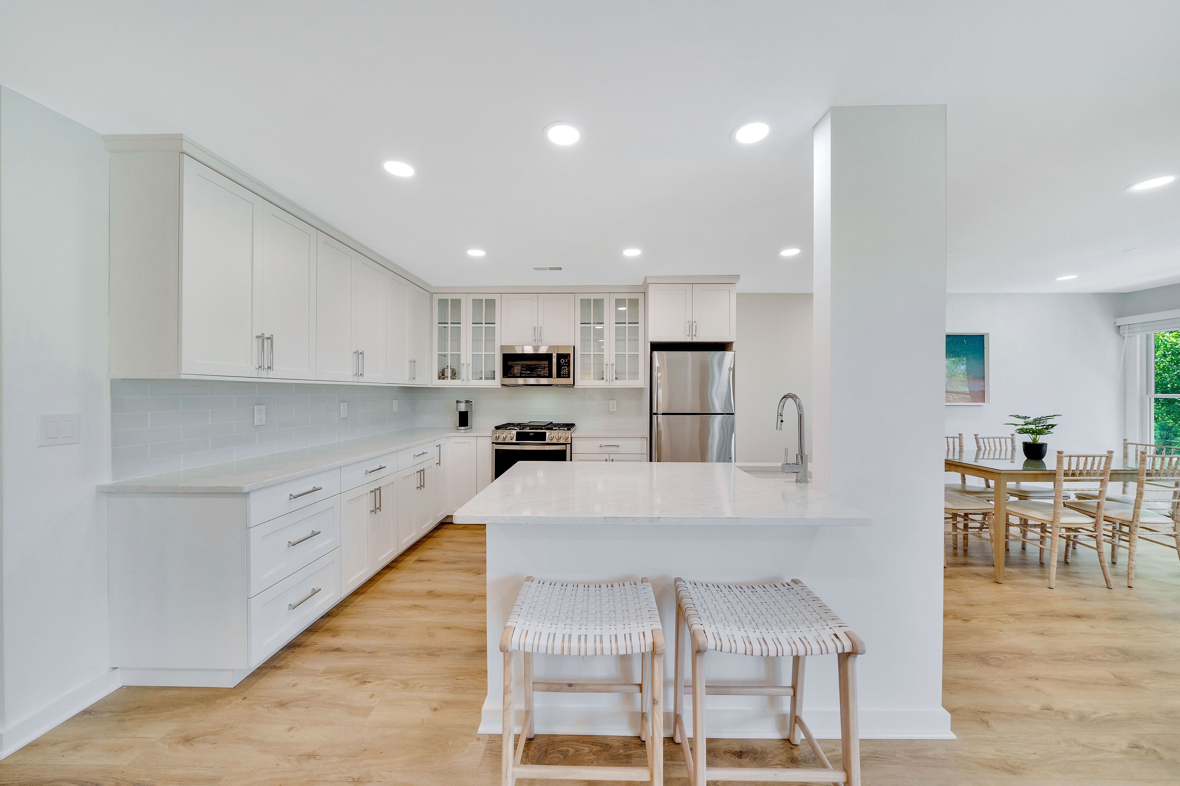 Cozinha moderna com armários brancos, uma ilha central e um espaço de refeições com cadeiras e mesa de madeira.