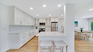 Cozinha moderna com armários brancos, uma ilha central e um espaço de refeições com cadeiras e mesa de madeira.