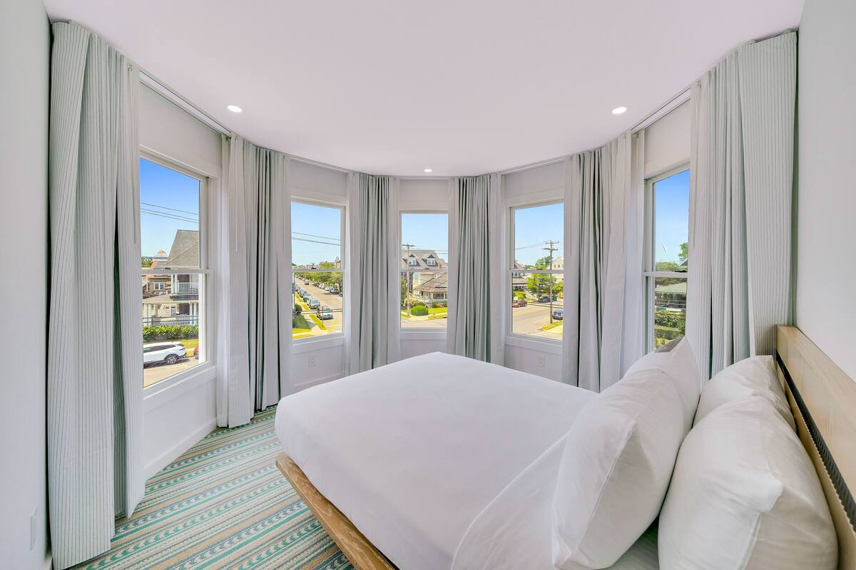 A hotel room with a large bed, multiple windows, and a view of the street.