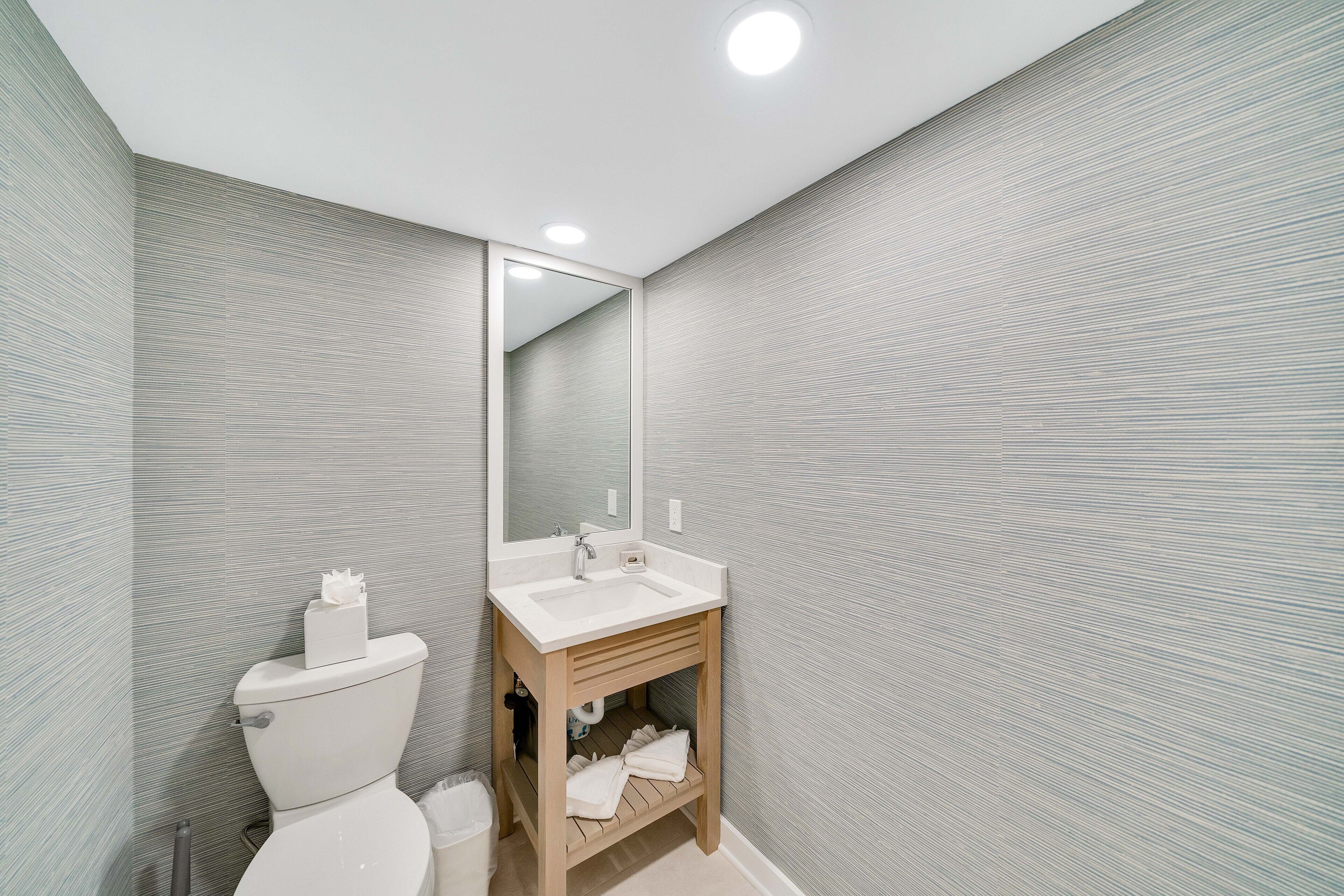 A modern bathroom with a white sink, mirror, and toilet.