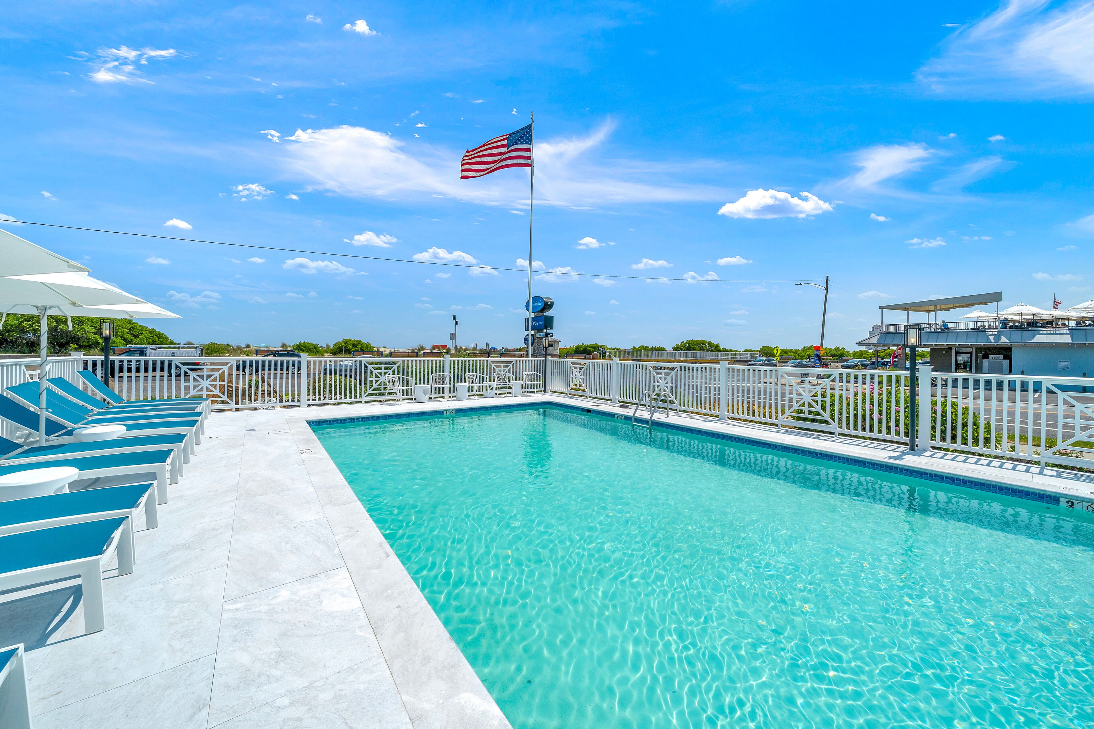 A swimming pool with a flag, lounge chairs, and a fenced area.