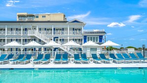 A hotel with a pool area featuring multiple lounge chairs and umbrellas.