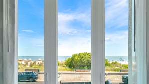 A view through a window with a beach in the background, including umbrellas and a bench.