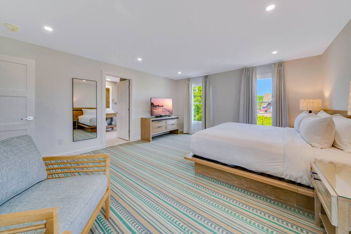 A modern hotel room with a large bed, a seating area with a sofa, a TV, and a view of the outdoors.