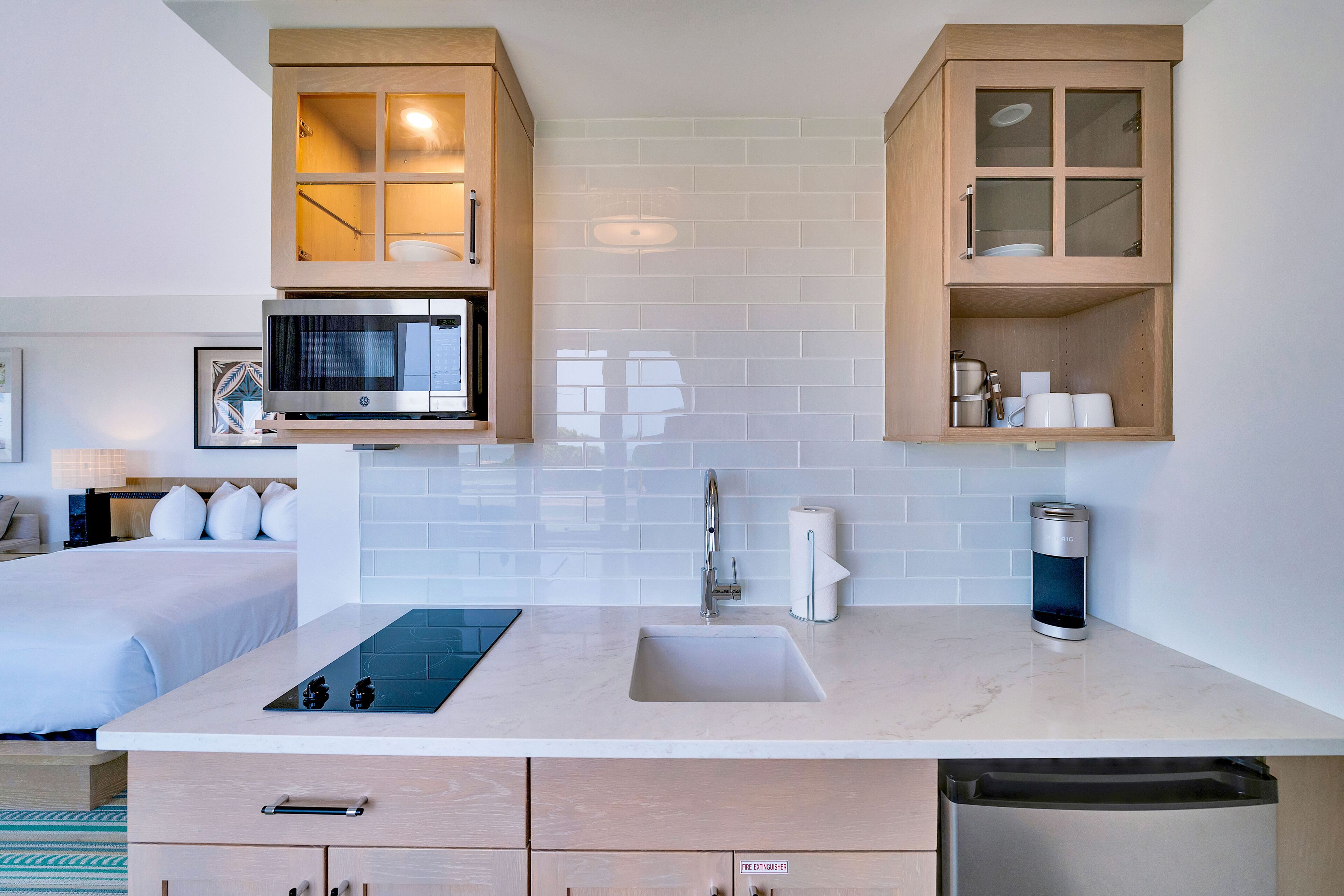 A modern kitchen with a built-in microwave, a sink, and a dishwasher. There are wooden cabinets with glass doors and a countertop with a kettle and a coffee maker.