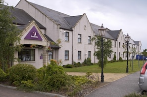 Un hôtel reconnaissable à son grand panneau « Premier Inn », doté d’une pelouse bien entretenue et présentant un style architectural classique.