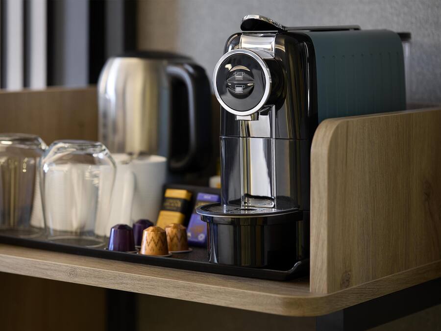 A coffee machine on a wooden counter with a tray of glasses and containers.