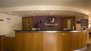 Hotellin vastaanottotiski, jossa on kaareva muotoilu, selkeästi näkyvä «Premier Inn» -kyltti ja tietokonenäyttö.