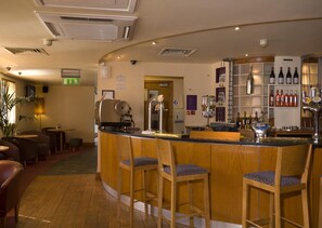 A bar area with wooden bar stools, a counter, and shelves with bottles. - Premier Inn Aberdeen City Centre (Aberdeen)