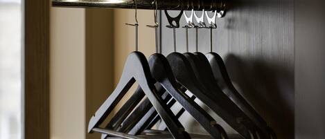 A metal rack with multiple hooks holding black items, likely coats or bags, in a room with a wooden door and a textured wall.