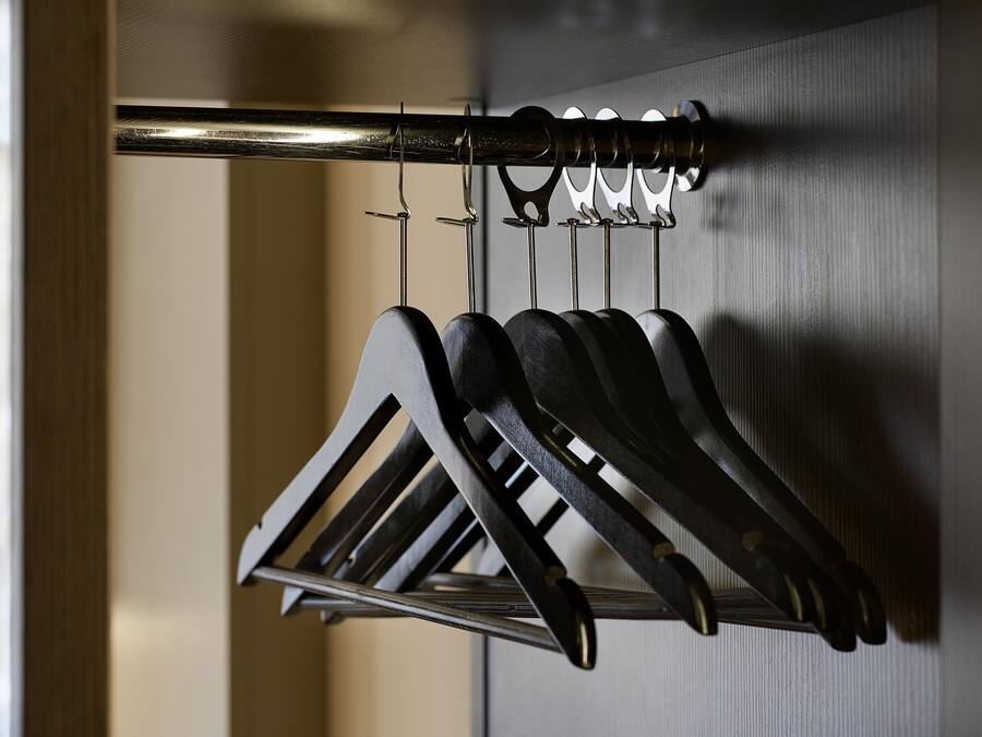 A metal rack with multiple hooks holding black items, likely coats or bags, in a room with a wooden door and a textured wall.