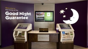 A check-in counter with two self-service kiosks, a digital screen, and a 'Check In' sign. - Premier Inn Aberdeen Airport - Dyce (Aberdeen)