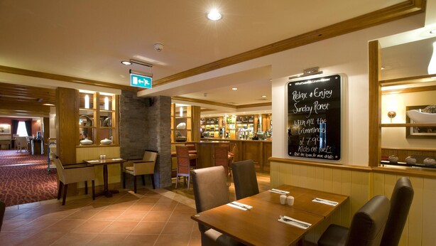 A restaurant with wooden tables and chairs, a bar area, and a chalkboard menu. - Premier Inn Lisburn (Lisburn)