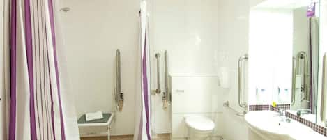 A bathroom with a shower, toilet, and sink, equipped with grab bars and a hand dryer.