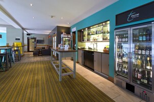 A hotel bar area with a bar counter, seating, and a minibar.