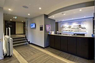 A hotel reception area with a counter, a television, and a staircase leading to another floor.