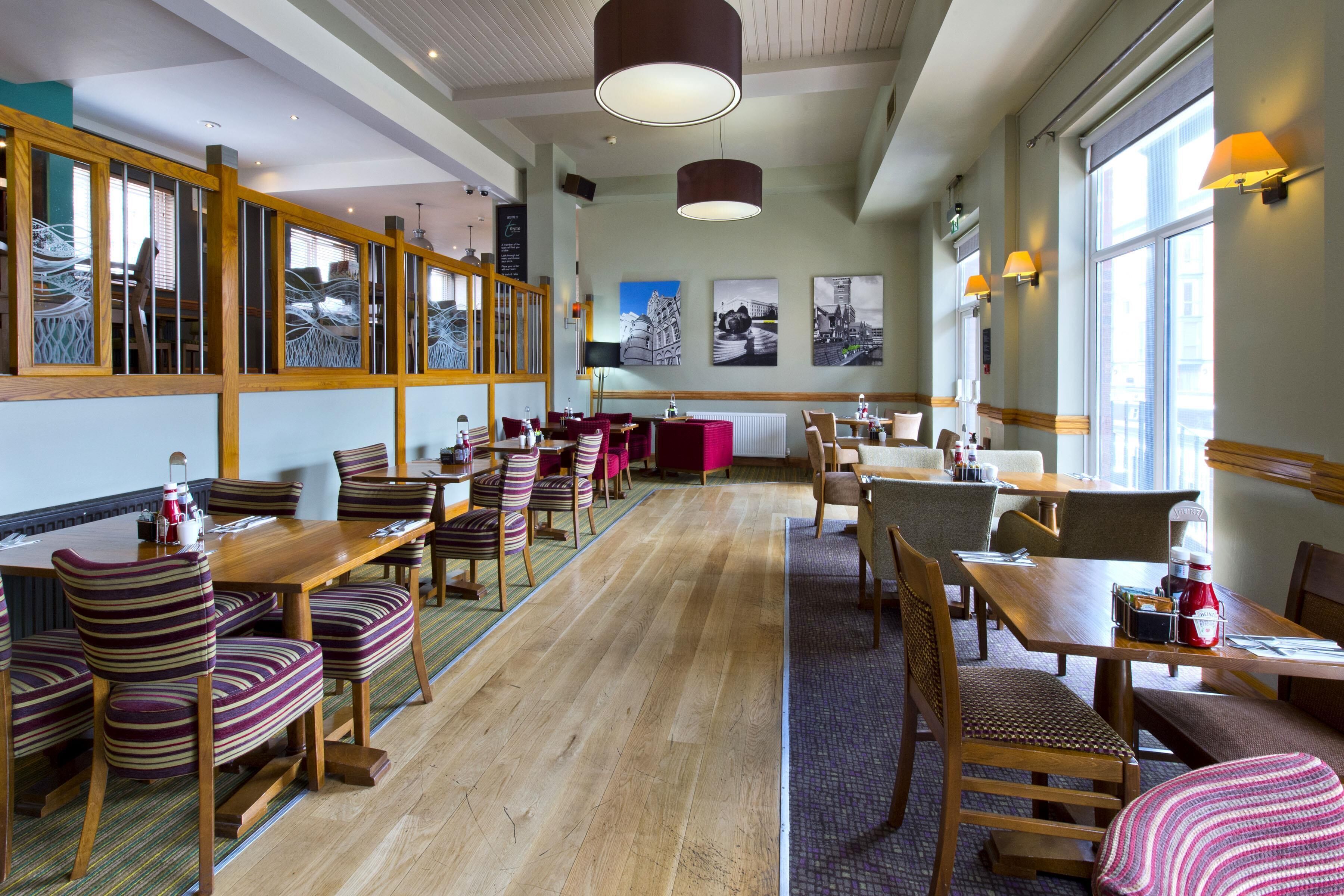A spacious dining area with wooden tables and striped chairs, large windows, and wall-mounted artwork.