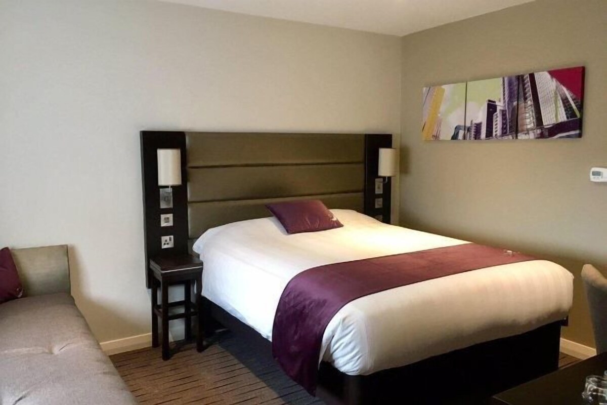 A hotel room with a single bed, a nightstand, a lamp, and a wall-mounted artwork.