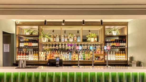 A bar area with shelves of various liquor bottles, a cash register, and a green bar counter. - Premier Inn Birmingham City - Aston (Birmingham)