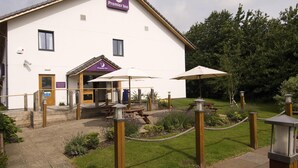 Un hôtel à l’extérieur blanc, avec une enseigne et un petit jardin agrémenté de tables de pique-nique et de parasols.