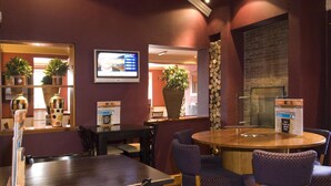 Un restaurant avec une table ronde en bois, des chaises violettes, un écran de télévision et un mur en briques.