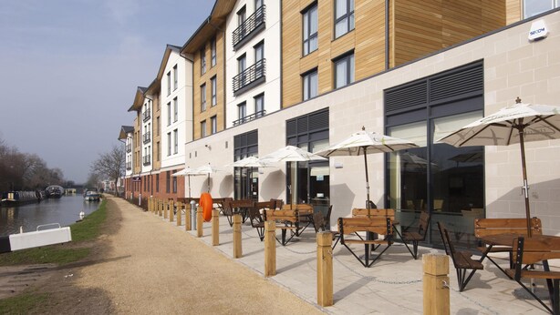 A riverside walkway with outdoor seating and a building with multiple floors and balconies.