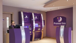 A hotel reception area with a check-in counter, a welcome sign, and a Premier Inn logo on the wall.