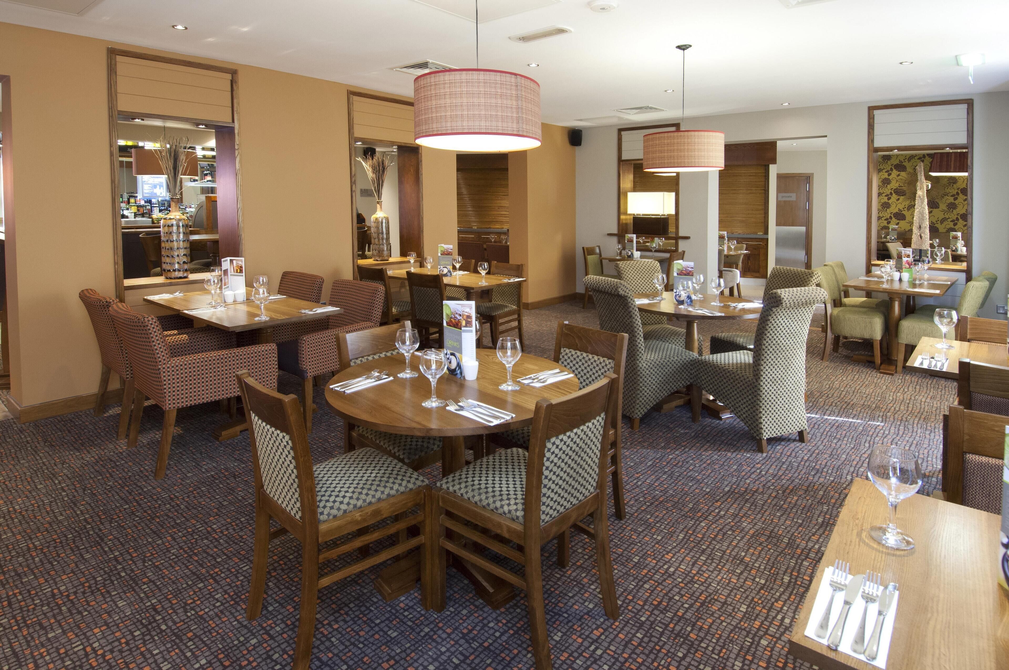 A hotel dining area with multiple round tables, chairs, and a large hanging light fixture.